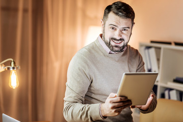 I like it. Cheerful brunette expressing positivity and holding tablet in both hands while chatting online
