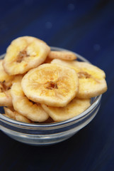 Healthy snack made from Banana Chips. Sliced Banana pieces in Glass bowl on Dark blue Background. Vertical Image.