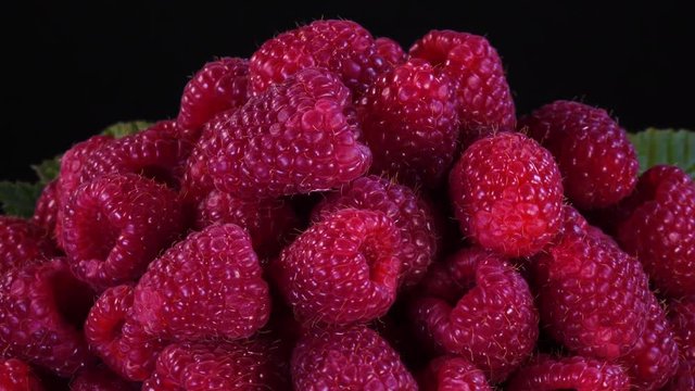 Closeup rotation of fresh ripe raspberries with leaves against black background in 4K.
