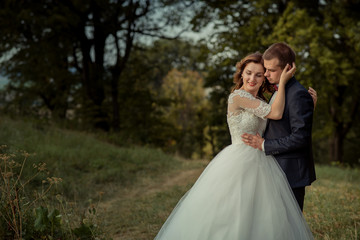 Romantic outdoor portrait. Stylish attractive newlywed couple is hugging and gorgeous bride is softly stroking the groom face. Forest location.