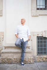 Young man caucasian leaning on a wall outdoor in the city looking away, smiling - customer, city living, positive feelings concept