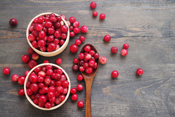 Fresh juicy cranberry in wooden round bowls with a wooden spoon on a table, close up