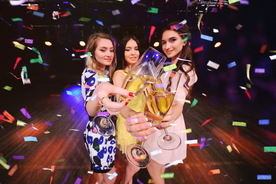 three pretty young girls with glasses of champagne having fun at a party in a nightclub.