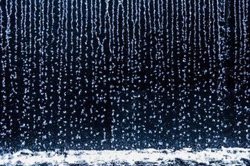 Rain droplets running down continuously on black background.
