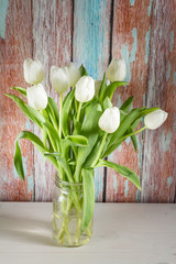 White tulips in glass jar. Wooden background.