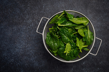 Fresh green spinach leaves on a dark concrete background, top view, flat lay, copy space.