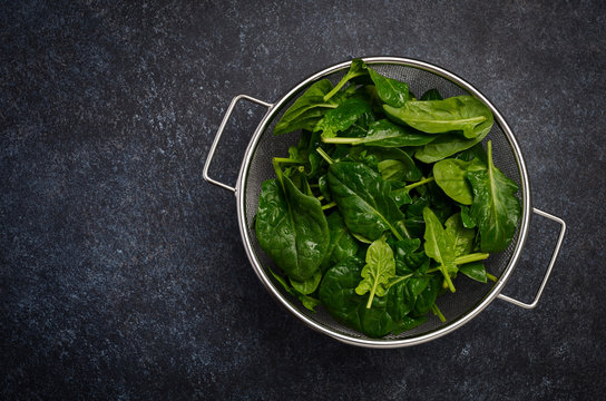 Fresh green spinach leaves on a dark concrete background, top view, flat lay, copy space.