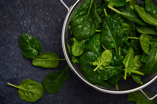 Fresh green spinach leaves on a dark concrete background, top view, flat lay.