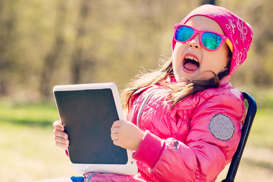 Little girl with tablet pc and headphones listening to music or watching video in summer park
