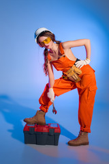 attractive girl in overalls uniform with tool belt and toolbox, on blue