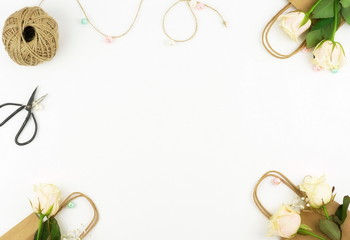 Feminine desk workspace frame with roses, green leaves, and gift bags on white background. Flat lay, top view. Flower background. Women's day, mother's day.