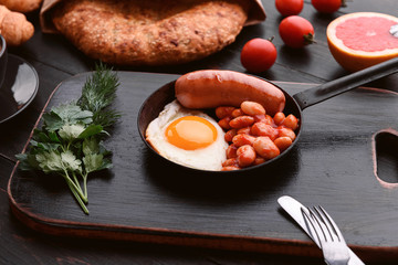 English breakfast. sausage, fried eggs and beans in tomato. coffee and bread nearby.