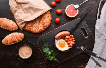 English breakfast. sausage, fried eggs and beans in tomato. coffee and bread nearby.
