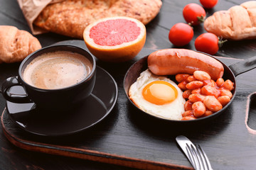 English breakfast. sausage, fried eggs and beans in tomato. coffee and bread nearby.