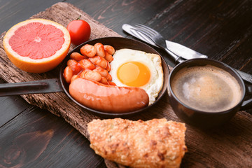 English breakfast. sausage, fried eggs and beans in tomato. coffee and bread nearby.