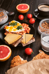 English breakfast. sausage, fried eggs and beans in tomato. coffee and bread nearby. chia with yogur and granola