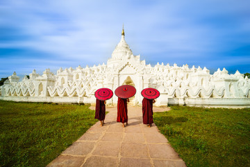 Three Asian young monk holding red umbrellas on the Mya Thein Tan Pagoda at Mingun, Mandalay...