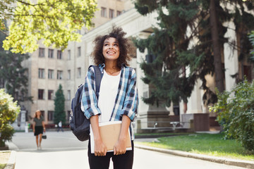 Student girl with backpack and workbooks at university building background