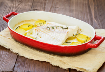 Fish cod baked in the oven with potatoes and spice and thyme - healthy diet healthy food. Dark brown wooden background, side view