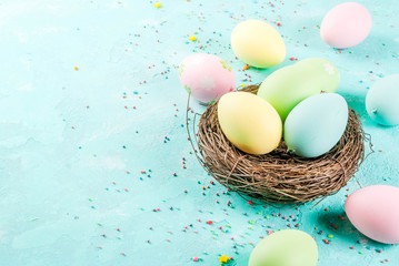 Multicolored Easter eggs with decorative bird's nest and sugar sprinkles on a light blue background,copy space