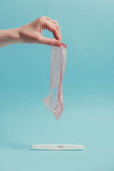 cropped shot of woman holding ripped condom in hand and pregnancy test isolated on blue