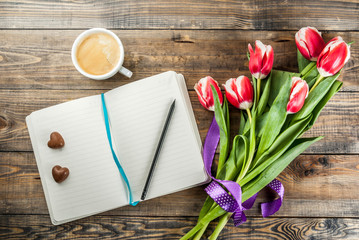 Valentines day background for congratulations, greeting cards. Fresh spring tulips flowers with notepad, chocolate hearts candy and coffee mug, on a wooden background top view copy space