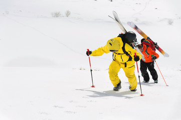 two ski freerider climbs the slope into deep snow powder with the equipment on the back fixed on the backpack.