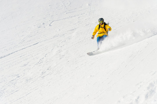 A man a snowboarder freerider descends a backcountry at high speed from a slope