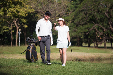 Asian young couple playing golf on golf course, the male partner is trainer to the female golfer