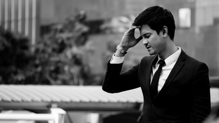 Frustrated Asian young business man standing in front of the office building. Black and white tone. copy space © ronnarong