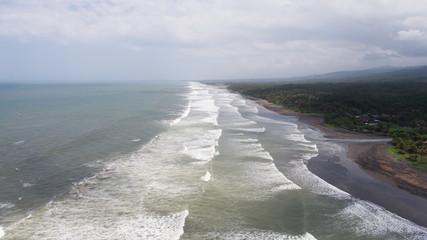 Tropical beach at cloudy weather. Aerial view of big waves on the beach with volcanic black sand in windy weather, Bali. Seascape Ocean, sky, sea. Travel concept. © Alex Traveler