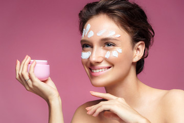 Obraz na płótnie Canvas Woman applying wrinkle cream or anti-aging skin care cream. Photo of smiling woman with healthy skin on pink background. Skin care concept