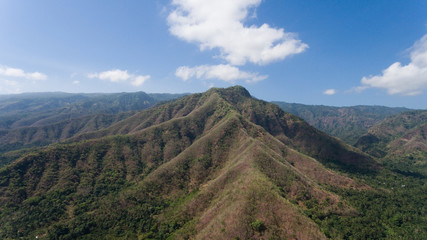 Fototapeta premium Aerial view of landscape, mountains covered with green forest, trees with sky and clouds, Bali,Indonesia. Slopes of the mountains are covered with forest in Asia. Travel concept.