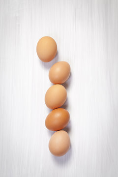 the Five yellow eggs lie in a line on a white wooden table