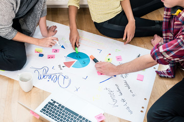Three young people analyzing pie chart and writing observations on a large paper sheet during...