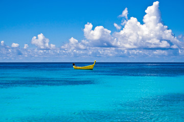 A distinctive yellow long-tail boat floating on the turquoise water at Ter Bay on Racha Island, Phuket, Thailand. 