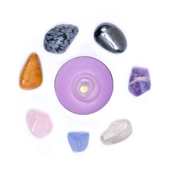 Lavender tea light candle surrounded by set of seven healing chakra stones for crystal healing, isolated on white background 