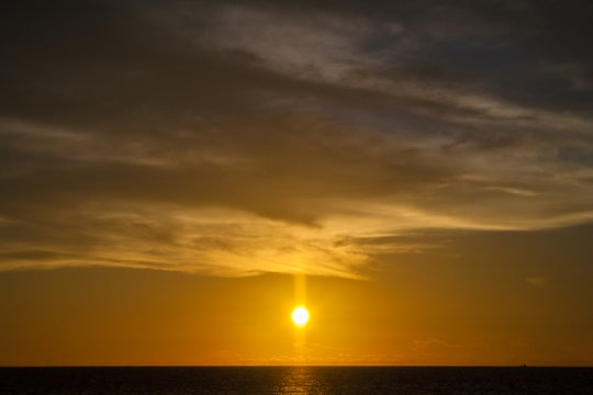 A special sunset; the sun is setting between a straight line horizon and a wall of clouds at Patok Beach on Racha Island, Phuket, Thailand.