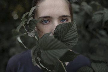 Face of Caucasian teenage girl behind leaves