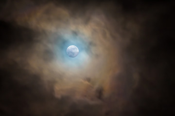 full bright moon in a dark sky, covered with clouds