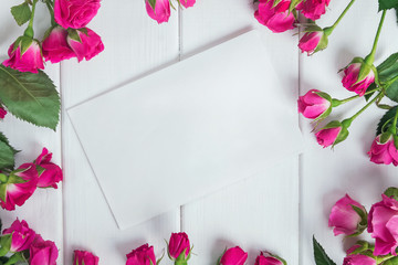 Pink roses and blank paper card on the white table