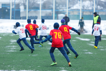 Young kids  football tournament - children play match on soccer field during the snow falling