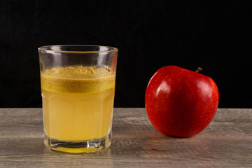 Red apple and a glass of freshly squeezed juice on a wooden background