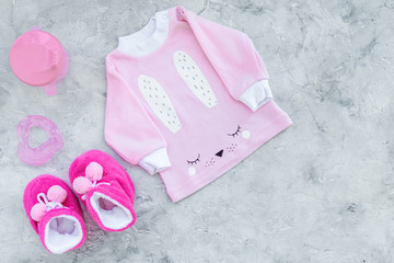 Cute pink baby clothes for girl. Shirt, booties, toy, bottle on grey background top view copy space