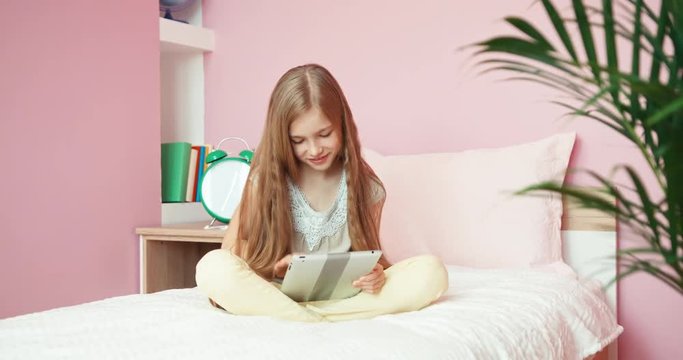 Girl with long blonde hair using tablet in bedroom