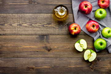 Obraz na płótnie Canvas Light salad dressing. Apple cider vinegar in bottle among fresh apples on dark wooden background top view copy space