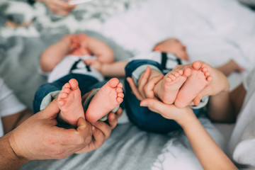 The legs of twin children in the hands of parents, Baby's feet. - obrazy, fototapety, plakaty