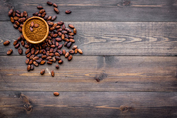 Main ingredient for chocolate. Cocoa powder in bowl near cocoa beans on dark wooden background top...