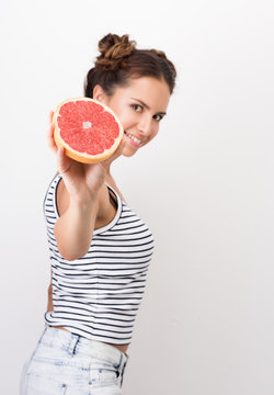 Freshness and vivacity. Young cheerful woman holding half a grapefruit at arm's length