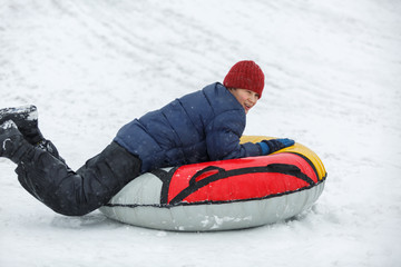 Fototapeta na wymiar kid sledding from a hill, makes snowballs and snowman on his winter holidays